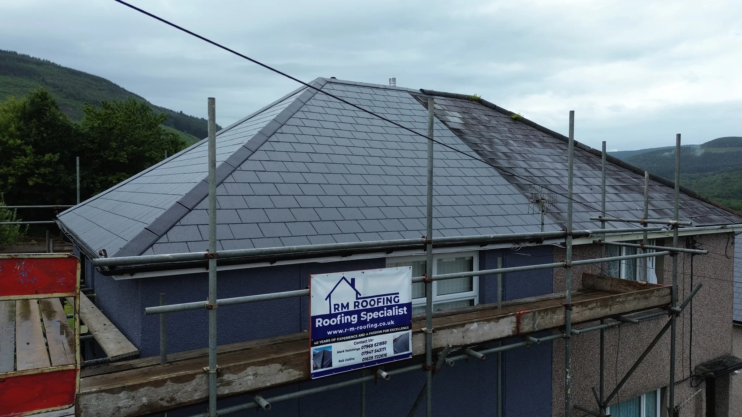 New slate hipped roof with RM Roofing banner on the scaffold, Neath