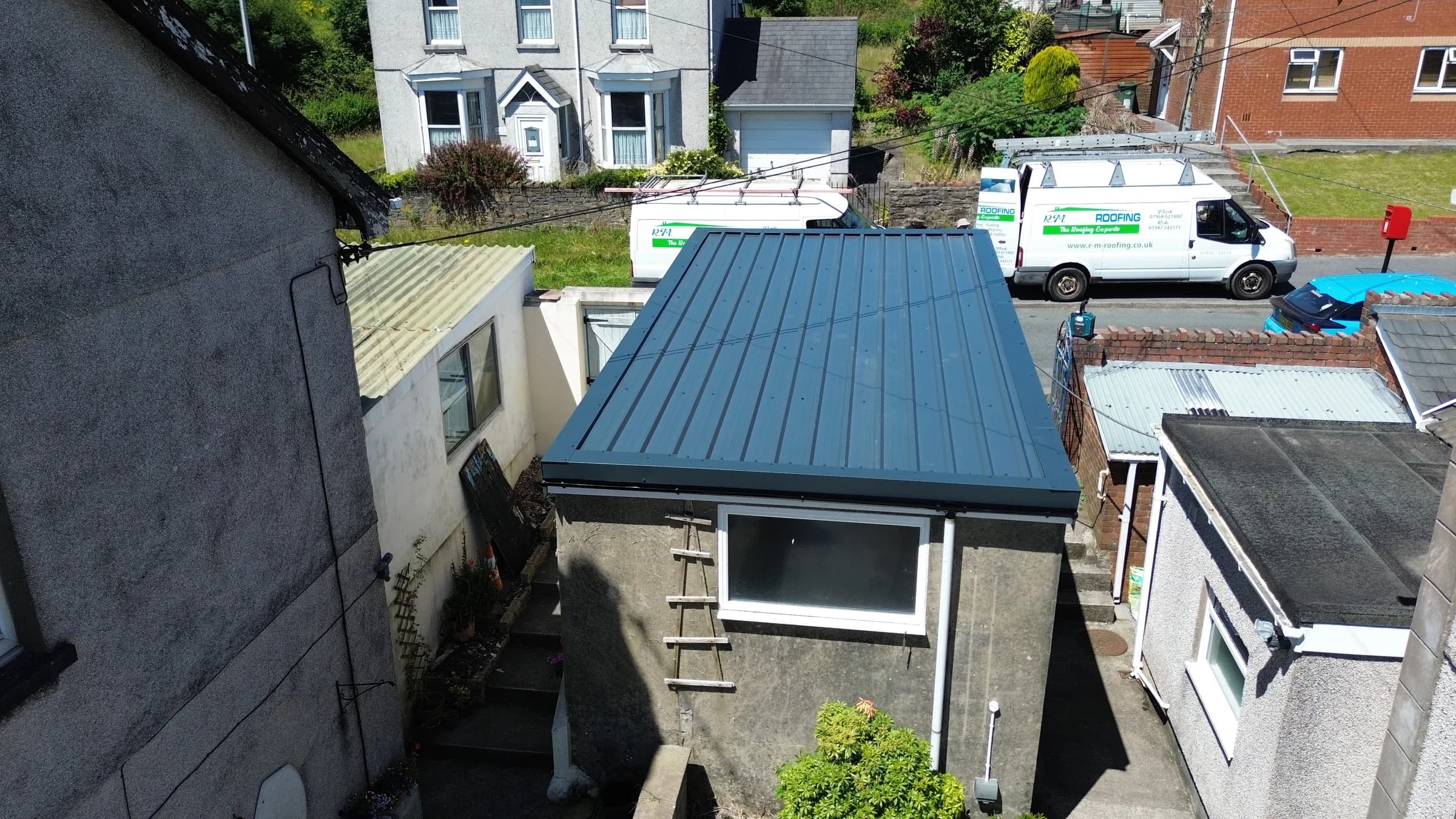 Standing seam metal roof on an outbuilding with RM Roofing vans on site, Neath